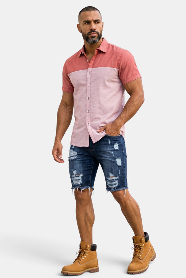 A man wearing a KIOKO Cityboy colorblock short-sleeve button-down shirt in pink and coral with distressed denim shorts.