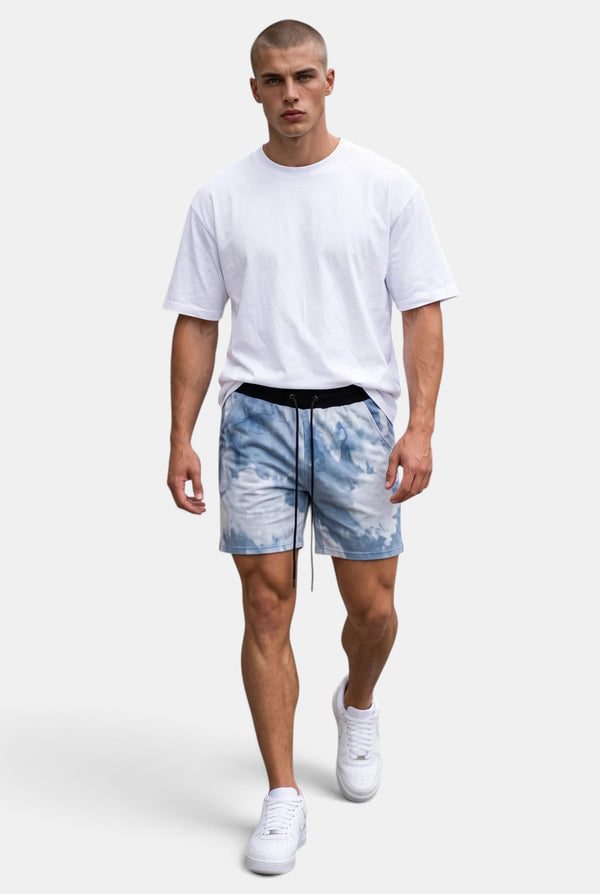 Model wearing KIOKO blue and white tie-dye cotton jogger shorts with a drawstring waist and a plain white t-shirt.