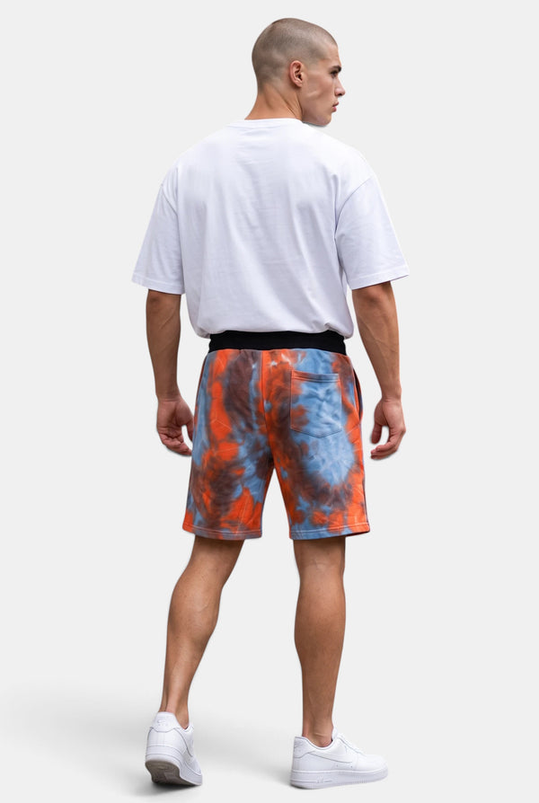 Back view of a man wearing KIOKO Cypher tie-dye jogger shorts in red and blue with an elastic waistband.