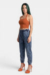 KIOKO Sculpt & Slay halter sports bra in rust orange, worn by a model with acid-wash blue joggers and orange heels.